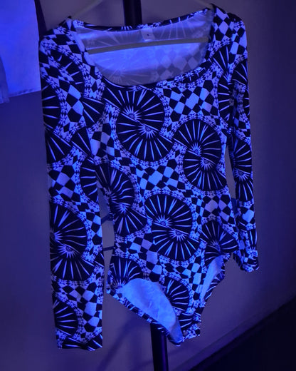 A long-sleeve bodysuit with a black and blue geometric pattern featuring circular fan and checkerboard motifs, hanging on a black hanger against a dark background under blue light.