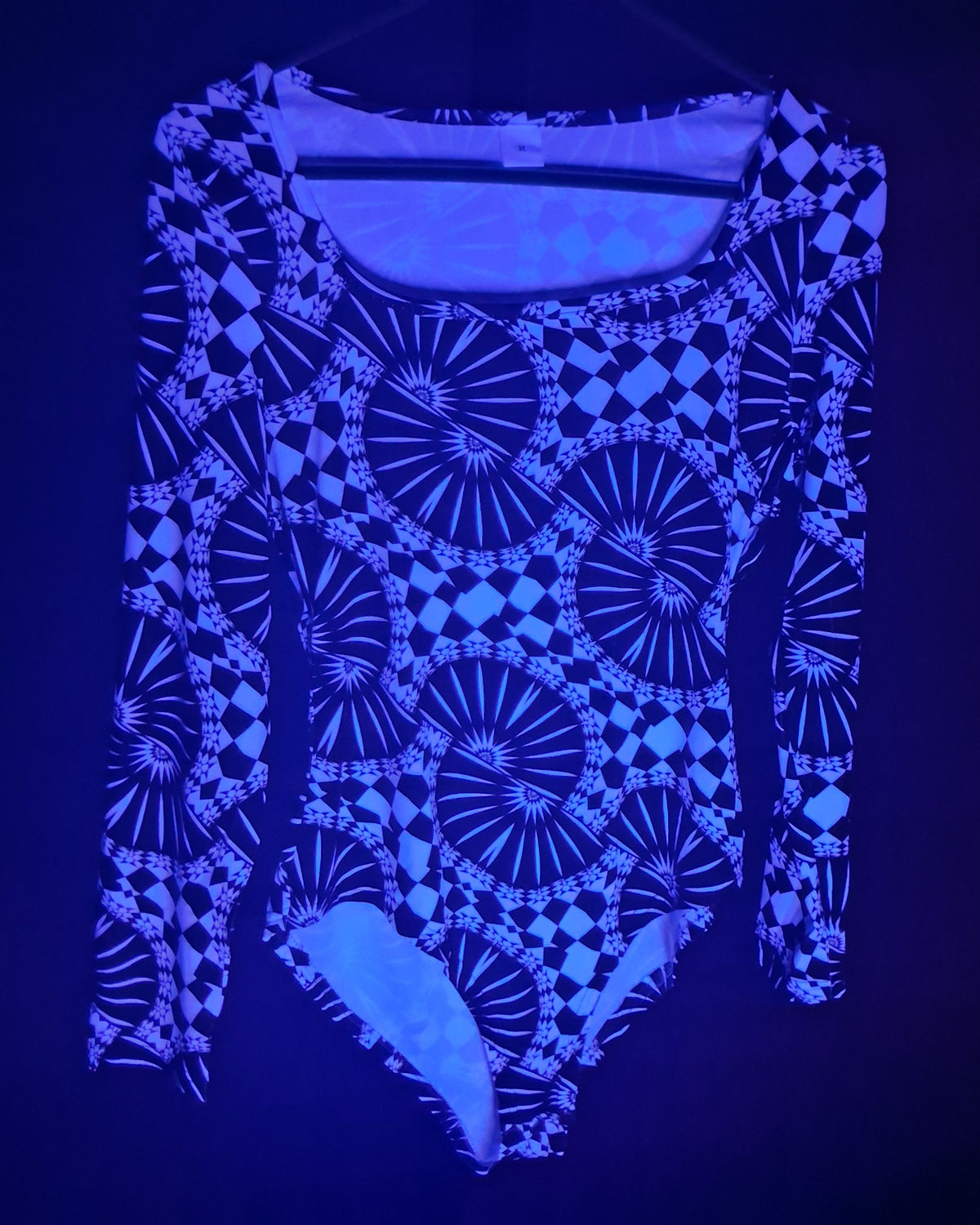 A long-sleeve bodysuit with a glowing blue and black geometric pattern, shown against a dark background under UV light.