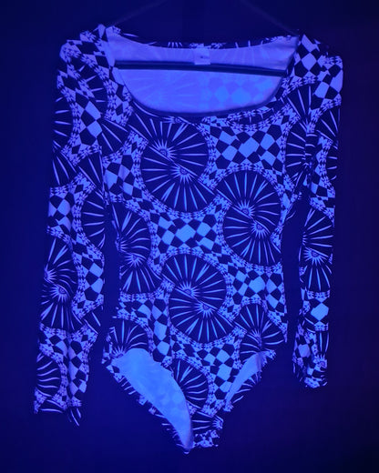 A long-sleeve bodysuit with a glowing blue and black geometric pattern, shown against a dark background under UV light.